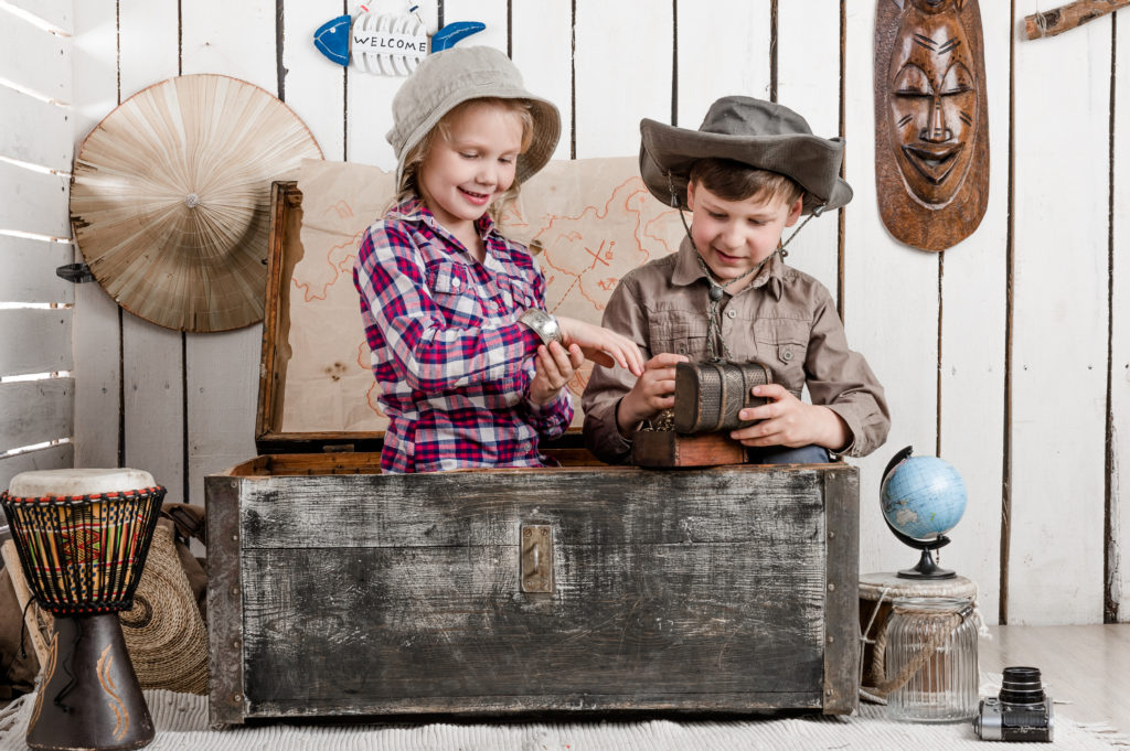 Smiling little boy and girl discovers treasure while sitting in big old chest