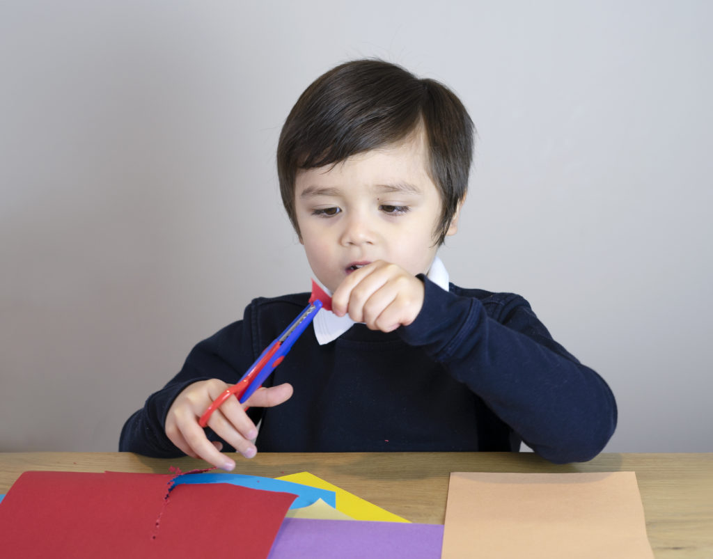 schoolboy showing how to use scissors cutting paper on white background with copy space, Kid boy using scissors cut easter egg in the class room, Children activities at school concept
